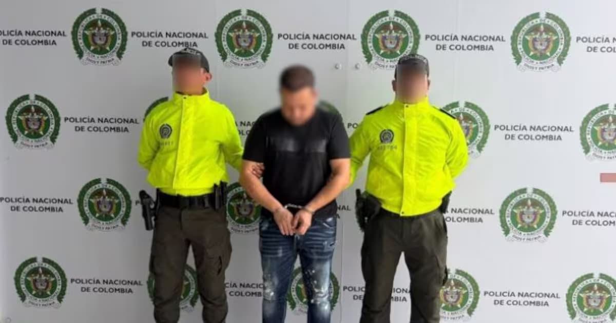 Dos policías custodian a Daneiro Correa Vega, alias El Señor, esposado frente a un panel de la Policía Nacional