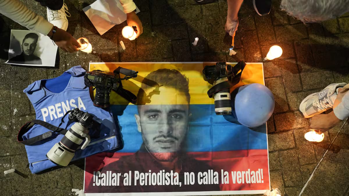 Velatón con un cartel del periodista Mateo Pérez sobre la bandera de Colombia, un chaleco de prensa y cámaras en el suelo