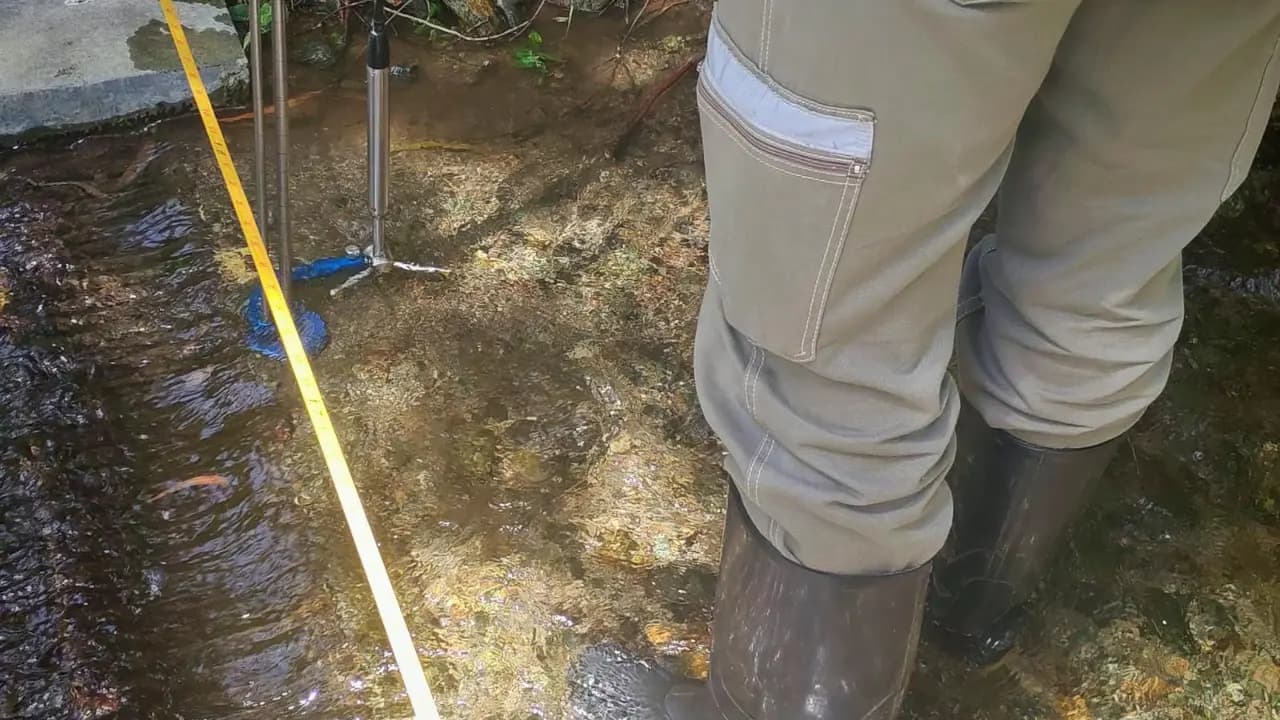 Un técnico con botas de caucho mide el caudal de una quebrada con un molinete hidrométrico