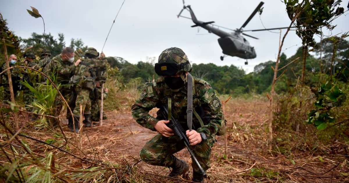 Un soldado del Ejército colombiano se agacha con su fusil en un claro de la selva mientras un helicóptero militar desciende al fondo