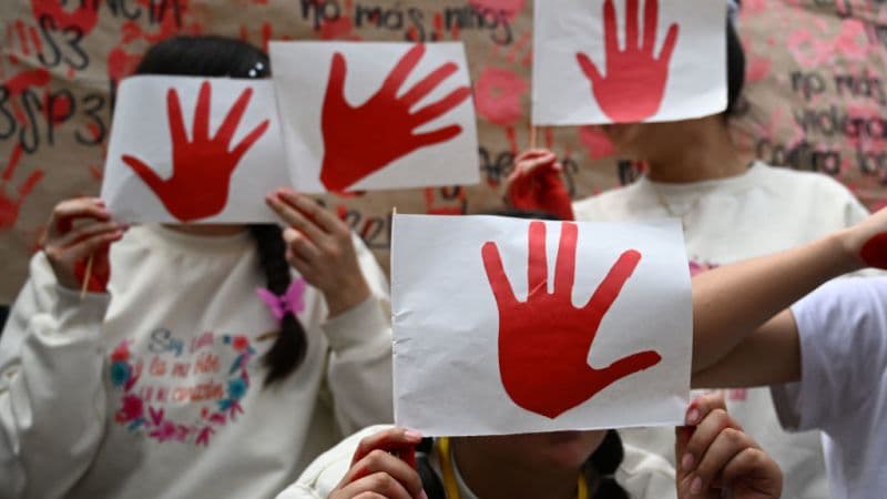 Varias niñas se cubren el rostro con carteles de una mano roja durante una jornada contra el reclutamiento infantil