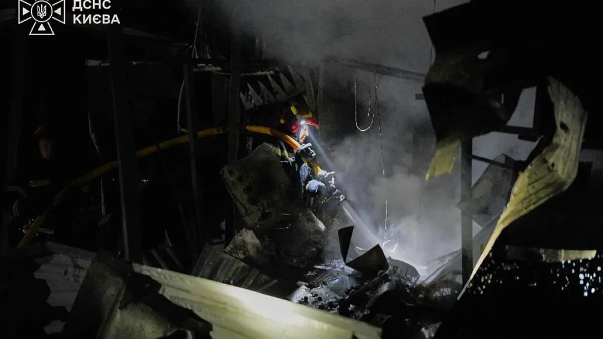 Tres hombres caminan por una calle de tierra junto a naves industriales calcinadas tras un bombardeo en Ucrania