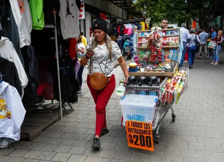 Una vendedora ambulante empuja su carro de mercancía por un andén del centro