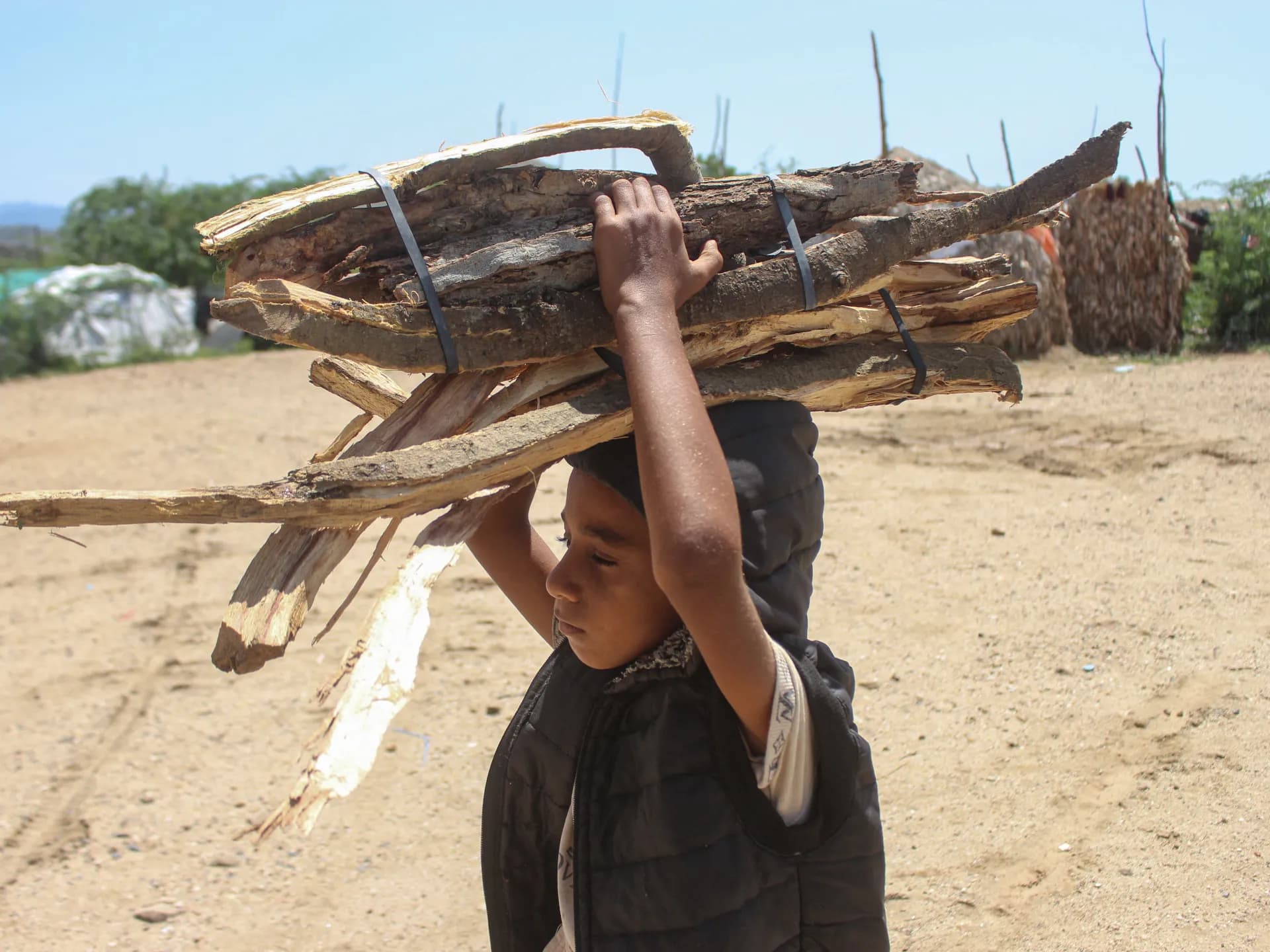 Un niño carga un atado de leña en un asentamiento de desplazados en Yemen