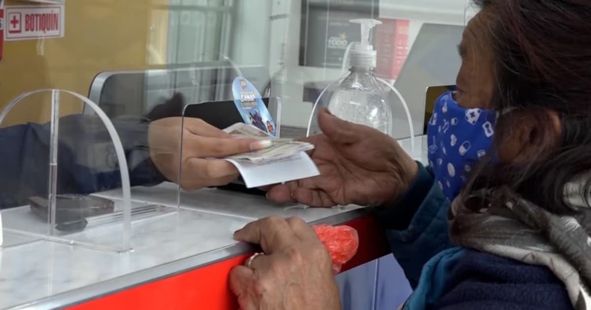 Personas hacen fila frente a un punto de pago de programas sociales