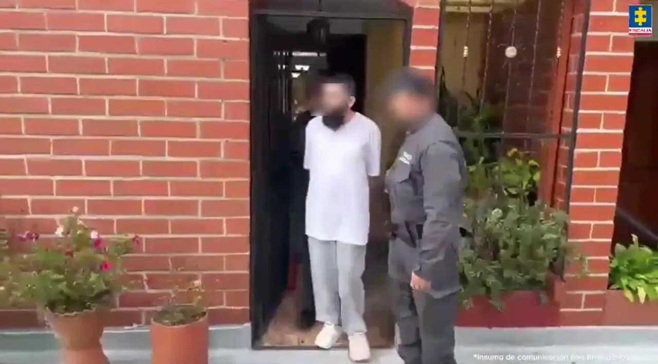 Un agente del CTI saca al detenido, con el rostro difuminado, de una vivienda de ladrillo en Envigado