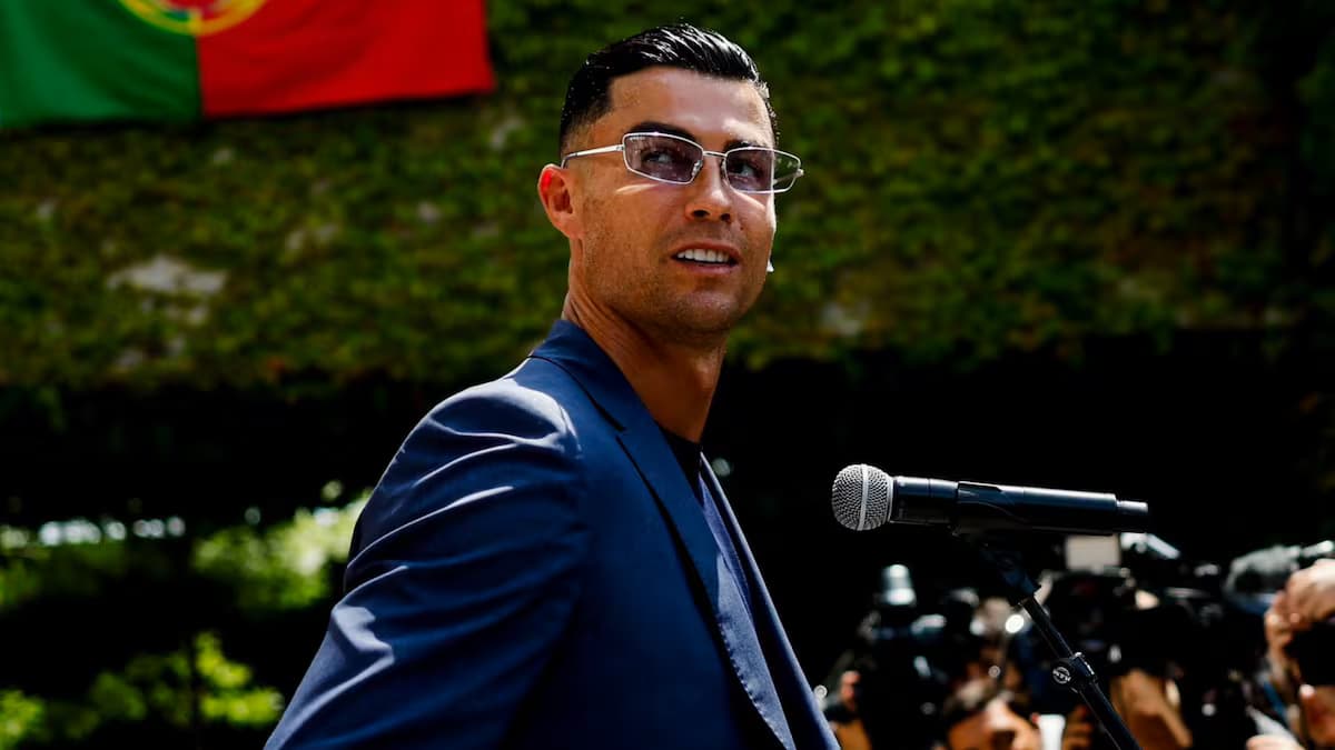 Cristiano Ronaldo, de traje azul y gafas, sonríe frente a un micrófono
