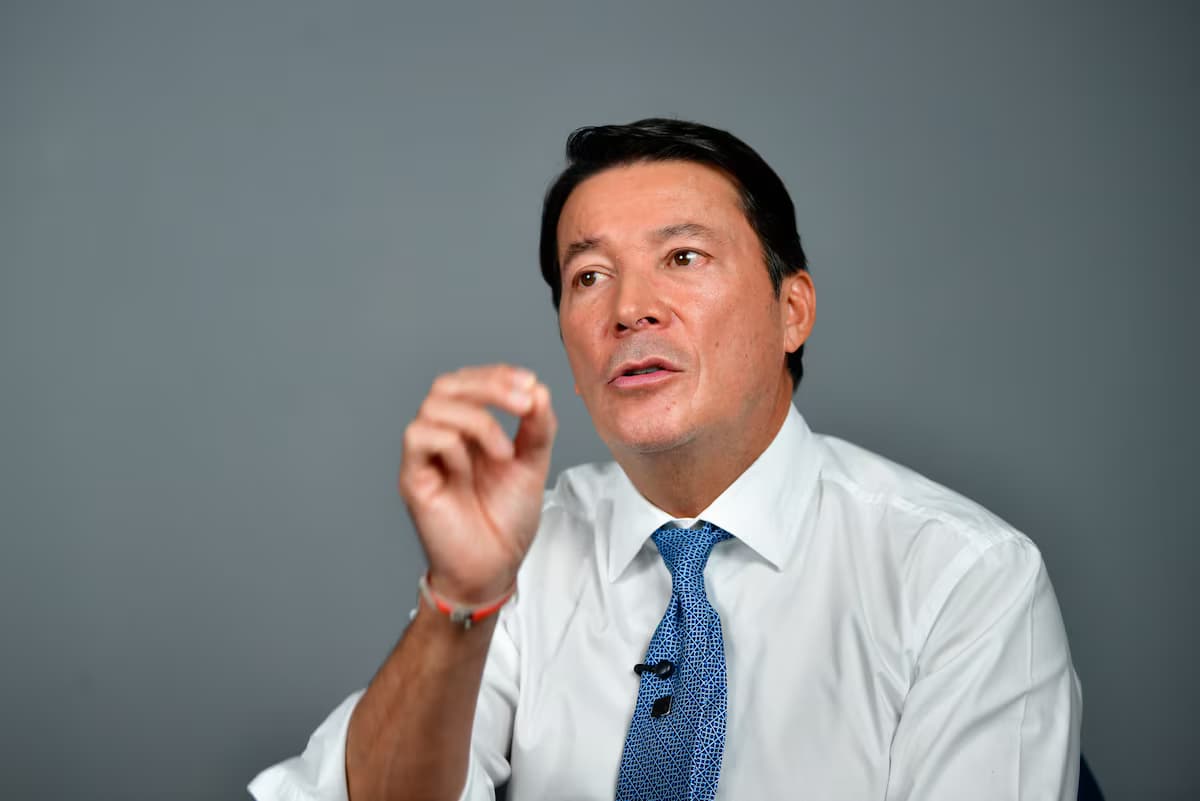 El registrador nacional Hernán Penagos, de camisa blanca y corbata azul, gesticula con la mano derecha mientras habla frente a un fondo gris