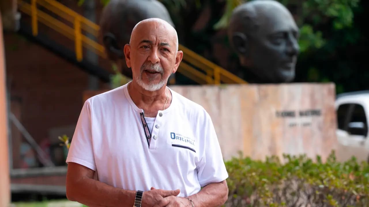 Leonardo Padura, de camiseta blanca, habla al aire libre frente a dos esculturas de cabezas de bronce