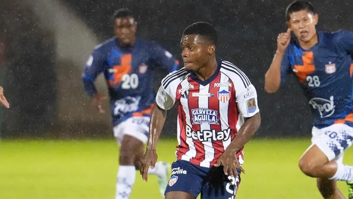 Un jugador de Junior conduce el balón bajo la lluvia ante futbolistas de Boyacá Chicó en Tunja