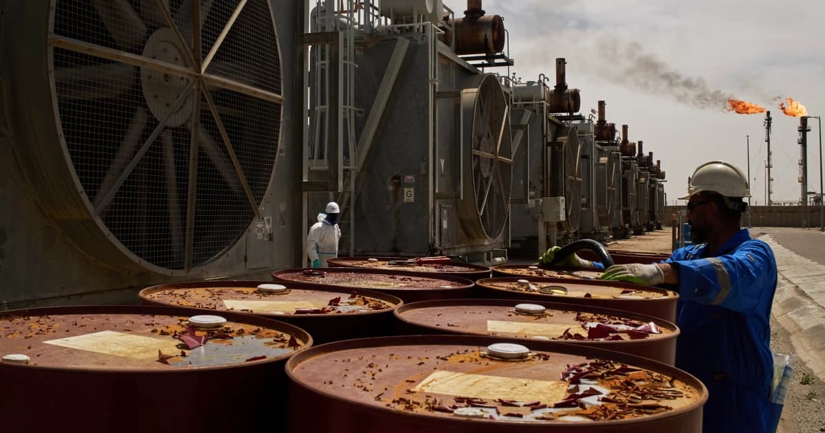 Operarios junto a bidones y torres de refrigeración en una instalación petrolera, con una antorcha de gas al fondo