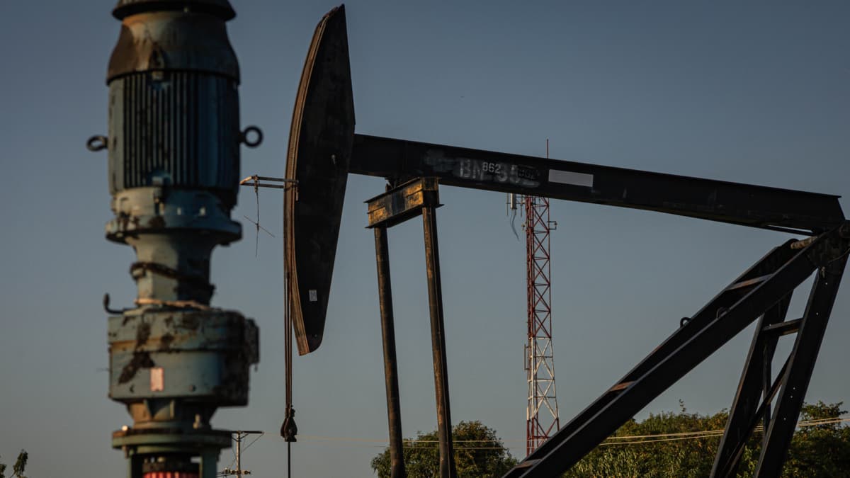 Un balancín de extracción de crudo recortado contra el cielo del atardecer en un campo petrolero