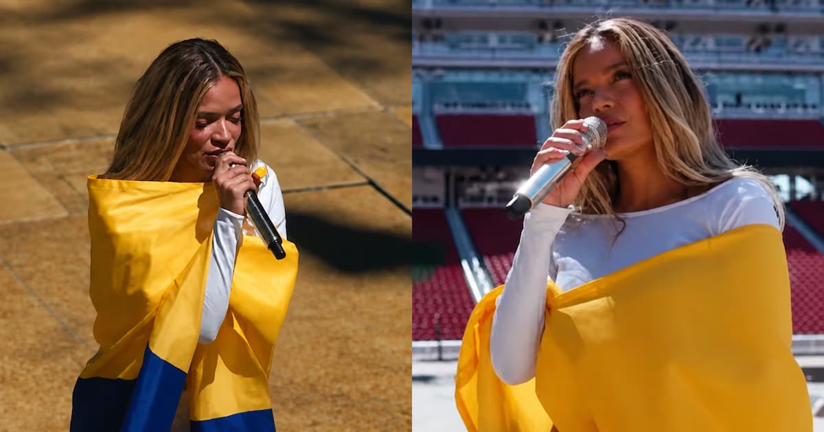 Karol G canta con un micrófono envuelta en una bandera de Colombia durante una presentación al aire libre