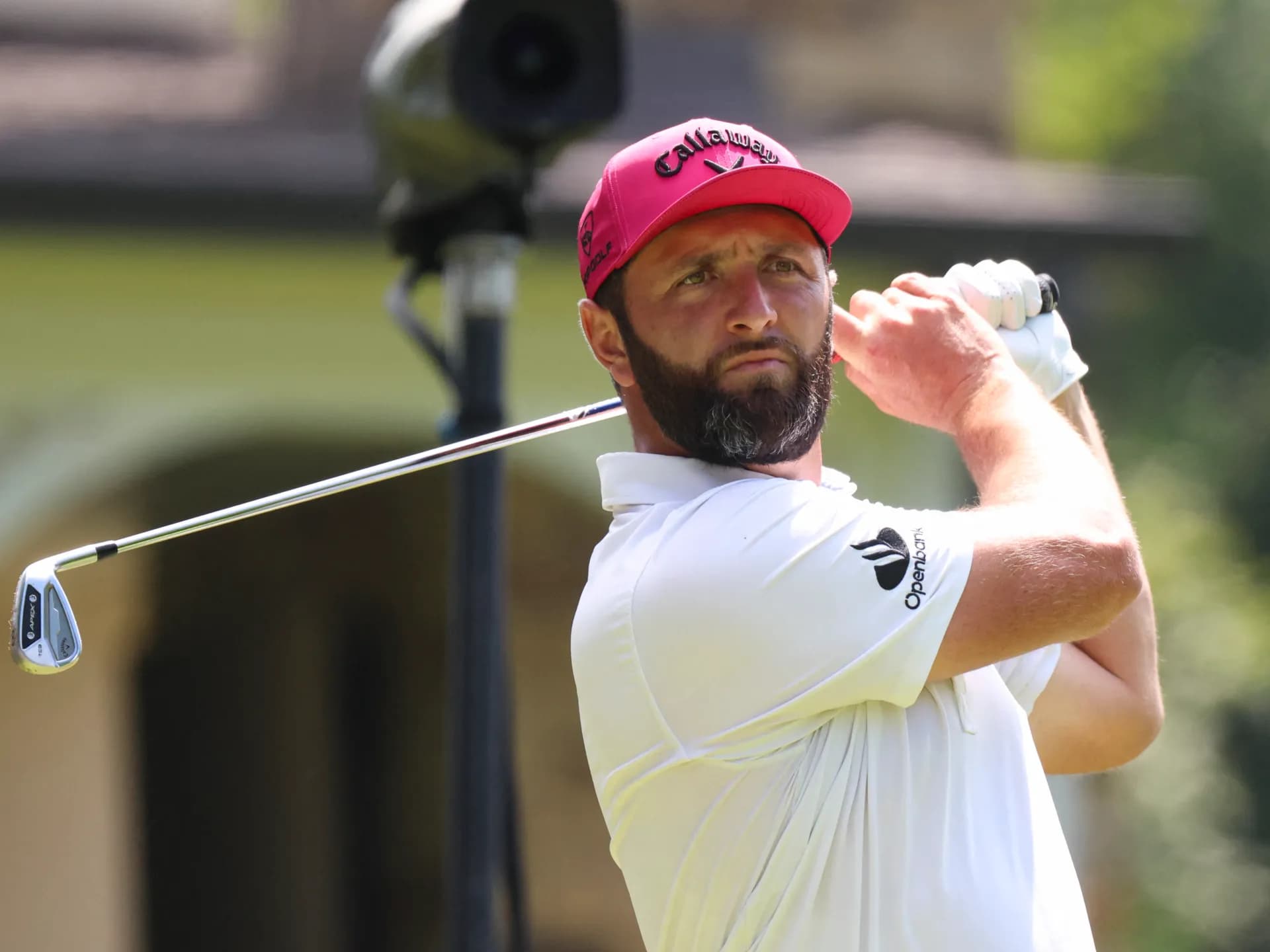 Jon Rahm, con gorra fucsia, sigue la trayectoria de un golpe con hierro durante un torneo del LIV Golf