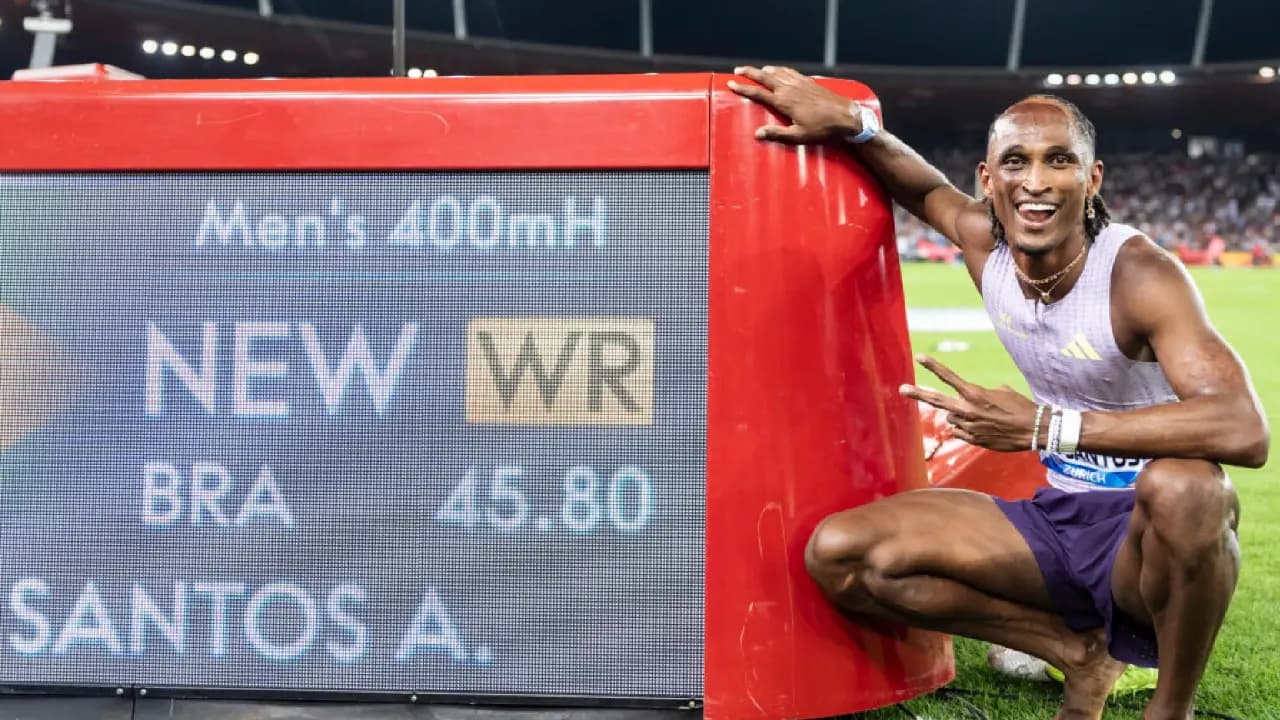 Un atleta sonriente se agacha junto a la pantalla del estadio que muestra el nuevo récord mundial de 45.80 en 400 metros vallas