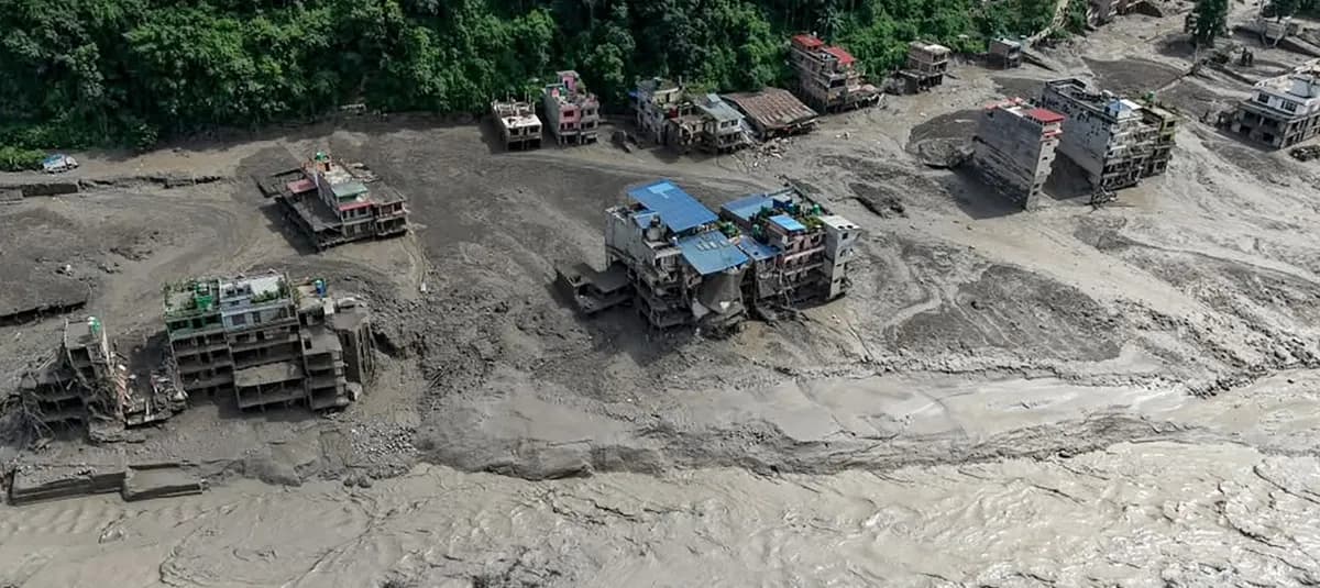 Vista aérea de un pueblo del Himalaya sepultado por el lodo, con edificios de varios pisos partidos y rodeados por un río de barro