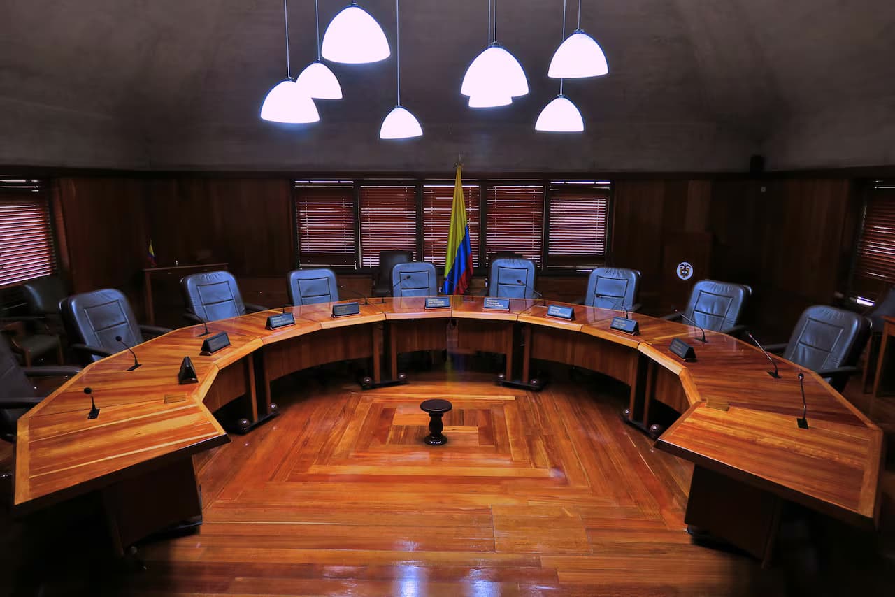 Sala de sesiones de la Corte Constitucional de Colombia con la mesa en semicírculo y la bandera nacional al fondo