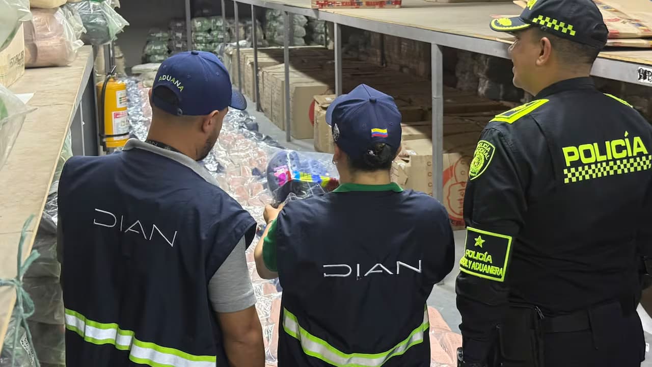 Funcionarios de la DIAN y un policía revisan mercancía aprehendida en una bodega de Cali