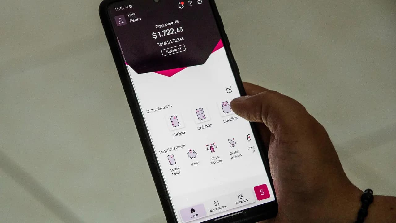 Una mano sostiene un teléfono celular con la aplicación de Nequi abierta en la pantalla de inicio