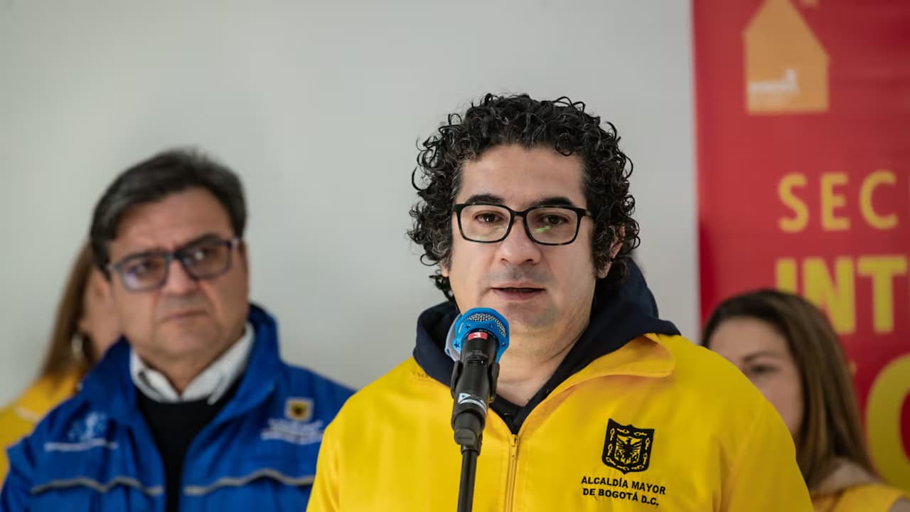 Roberto Angulo habla ante un micrófono con la chaqueta de la Alcaldía de Bogotá
