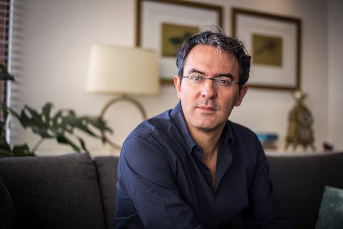 Retrato del escritor Juan Gabriel Vásquez sentado en un sofá, con gafas y camisa oscura