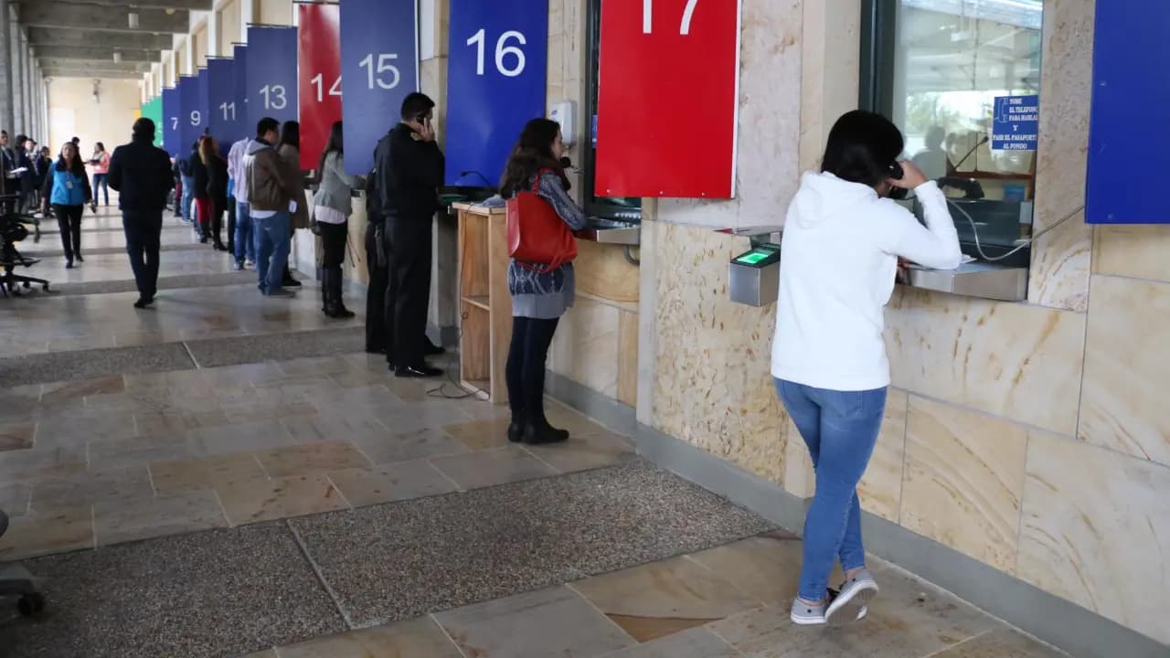 Personas hacen fila frente a las ventanillas numeradas de una oficina de trámites migratorios