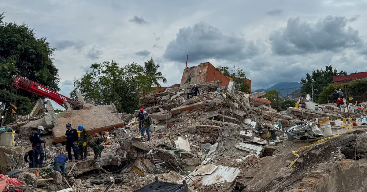 Socorristas con cascos caminan sobre una montaña de escombros de losas de concreto donde antes había edificios