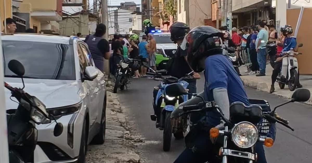 Curiosos y motociclistas en la calle donde ocurrió el ataque, con una patrulla de la Policía al fondo