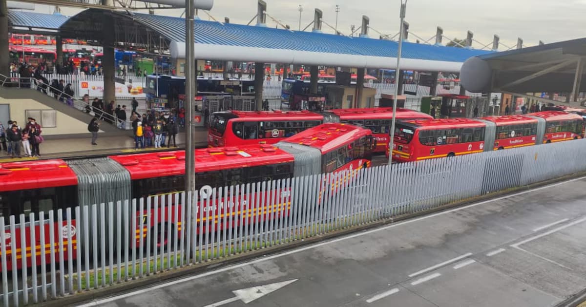 Buses rojos de TransMilenio detenidos en fila dentro de un portal, con usuarios esperando en la plataforma