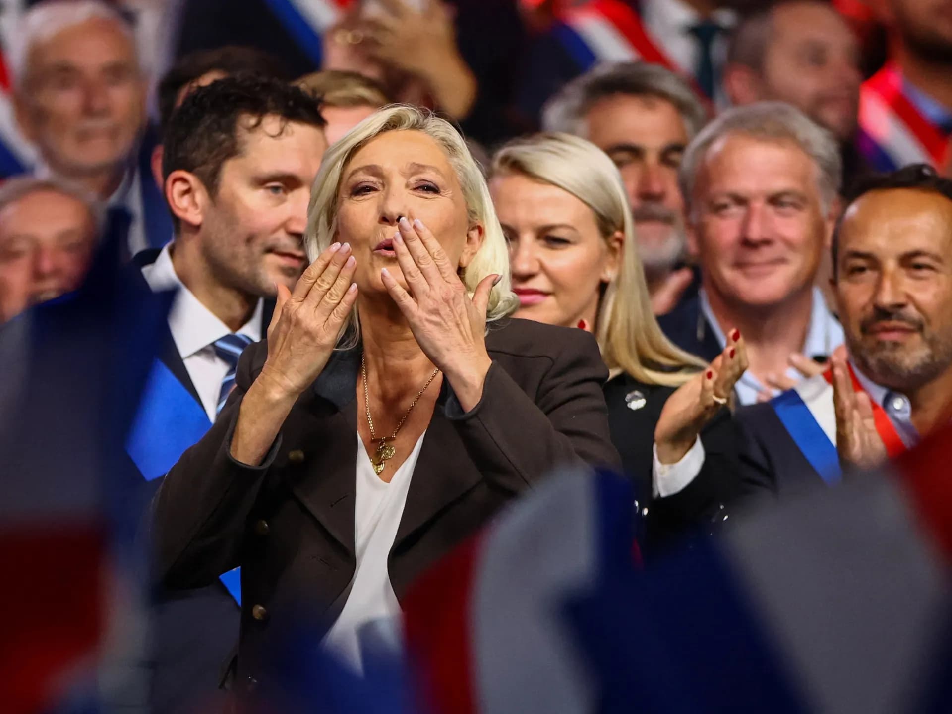 Marine Le Pen lanza besos al público rodeada de cargos electos con banda tricolor en un acto del Reagrupamiento Nacional