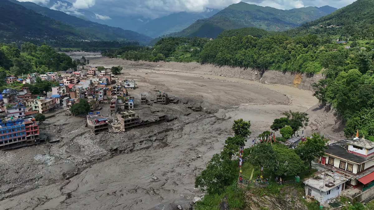 Vista aérea de un pueblo nepalí con edificios destruidos junto al cauce de lodo dejado por la riada