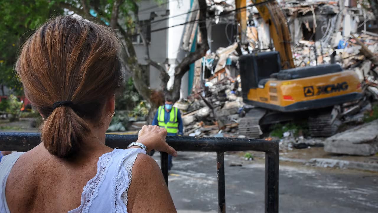Una mujer de espaldas observa una retroexcavadora que demuele un edificio