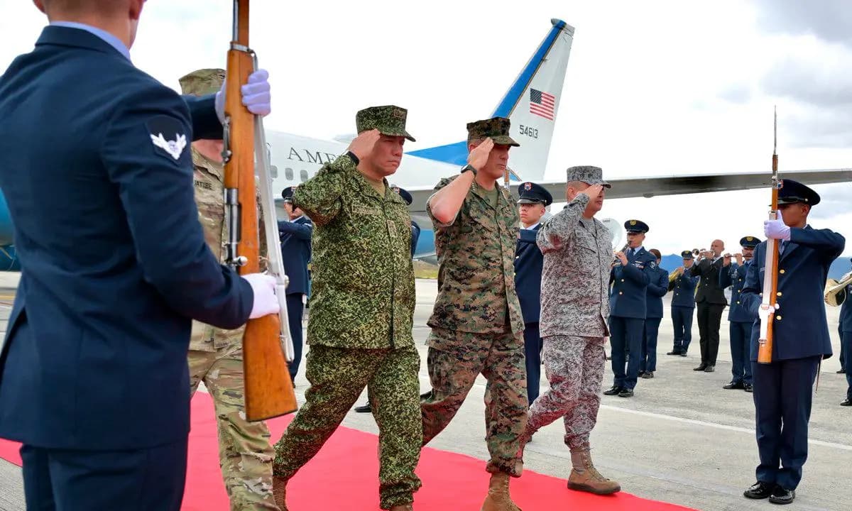 Oficiales militares colombianos y estadounidenses saludan mientras caminan sobre una alfombra roja en la pista, junto a un avión de la Fuerza Aérea de Estados Unidos