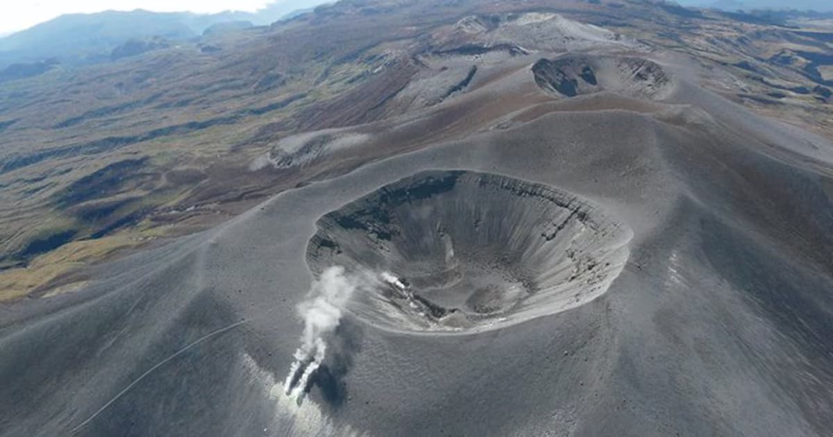Vista aérea del cráter del volcán Puracé, un cono gris de laderas desnudas con fumarolas blancas saliendo por una fisura en la base