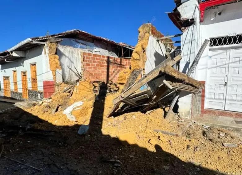 Una vivienda de tapia derrumbada sobre la calle de un pueblo antioqueño, con los muros de barro partidos y las vigas de madera caídas entre los escombros