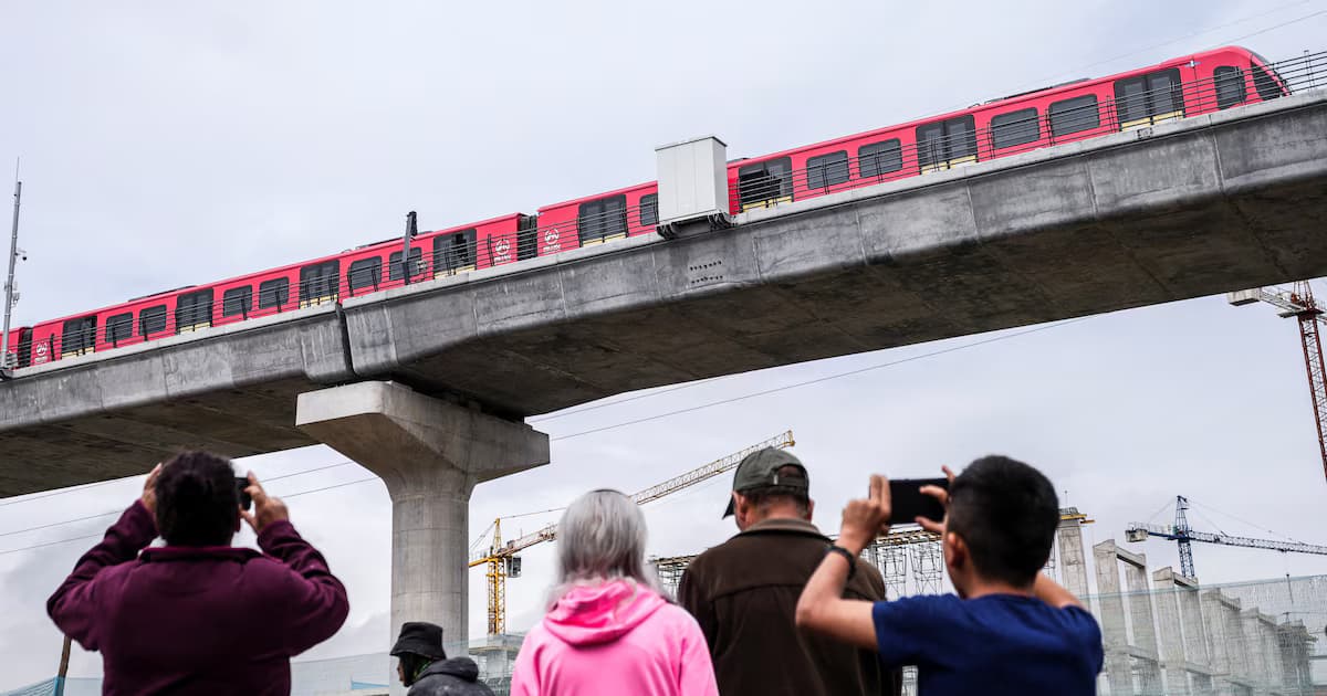 Un tren del metro de Bogotá recorre el viaducto mientras varias personas lo fotografían