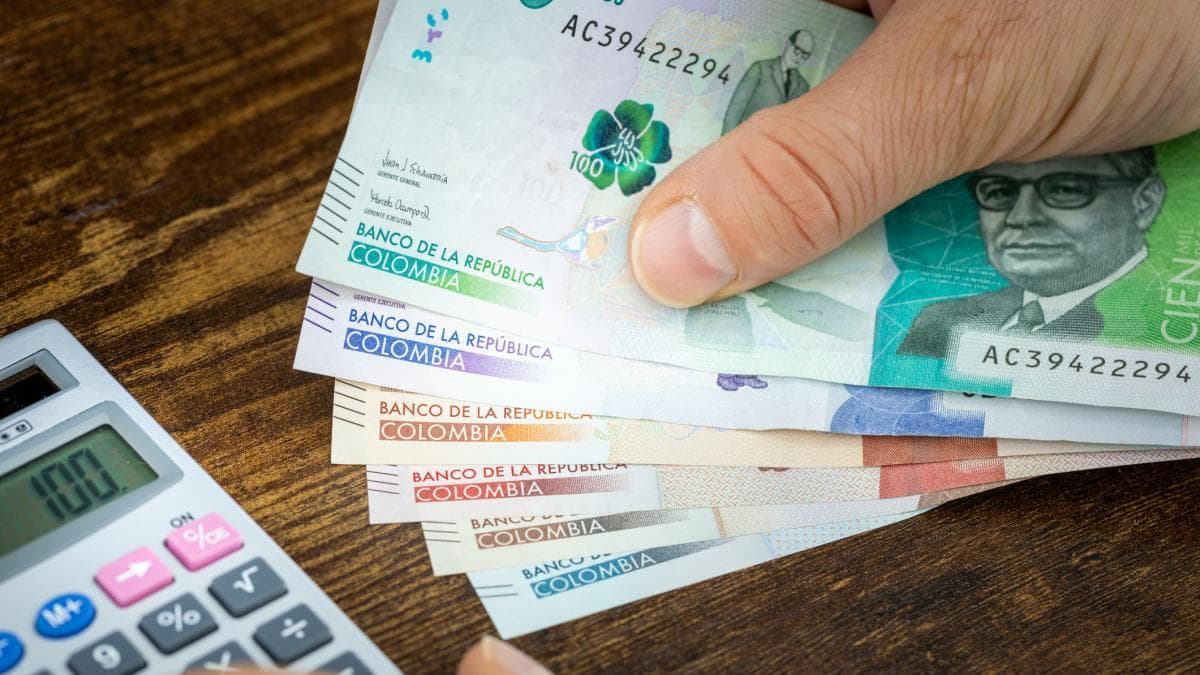 Una persona sostiene billetes de pesos colombianos junto a una calculadora