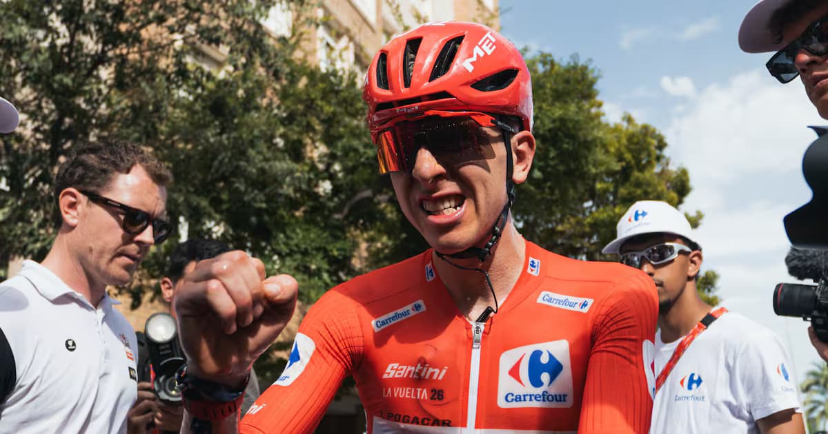 Tadej Pogacar, con casco y gafas rojas y el maillot rojo de líder de la Vuelta a España, aprieta el puño rodeado de auxiliares y cámaras tras una etapa