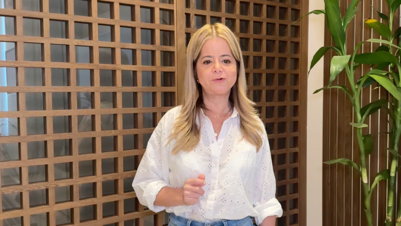 La ministra de Transporte, Elsa Noguera, habla de pie frente a un panel de madera con una planta a un costado