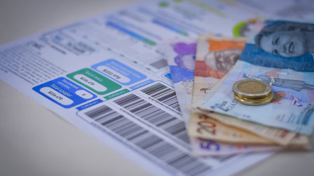 Una factura de servicios públicos sobre una mesa junto a billetes y monedas colombianas