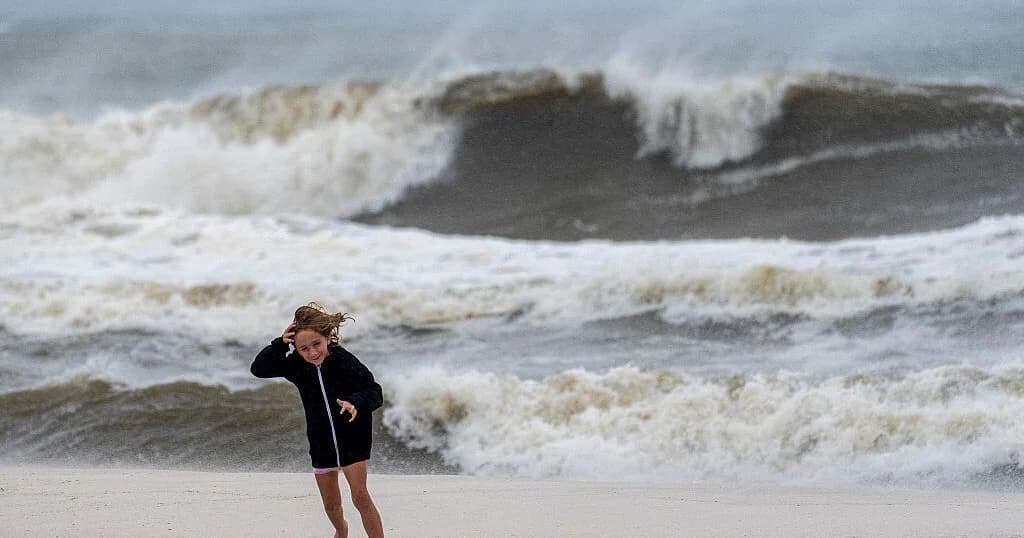 Una niña camina por la playa contra el viento frente a un mar agitado por el paso del huracán Isaías en la costa del Golfo