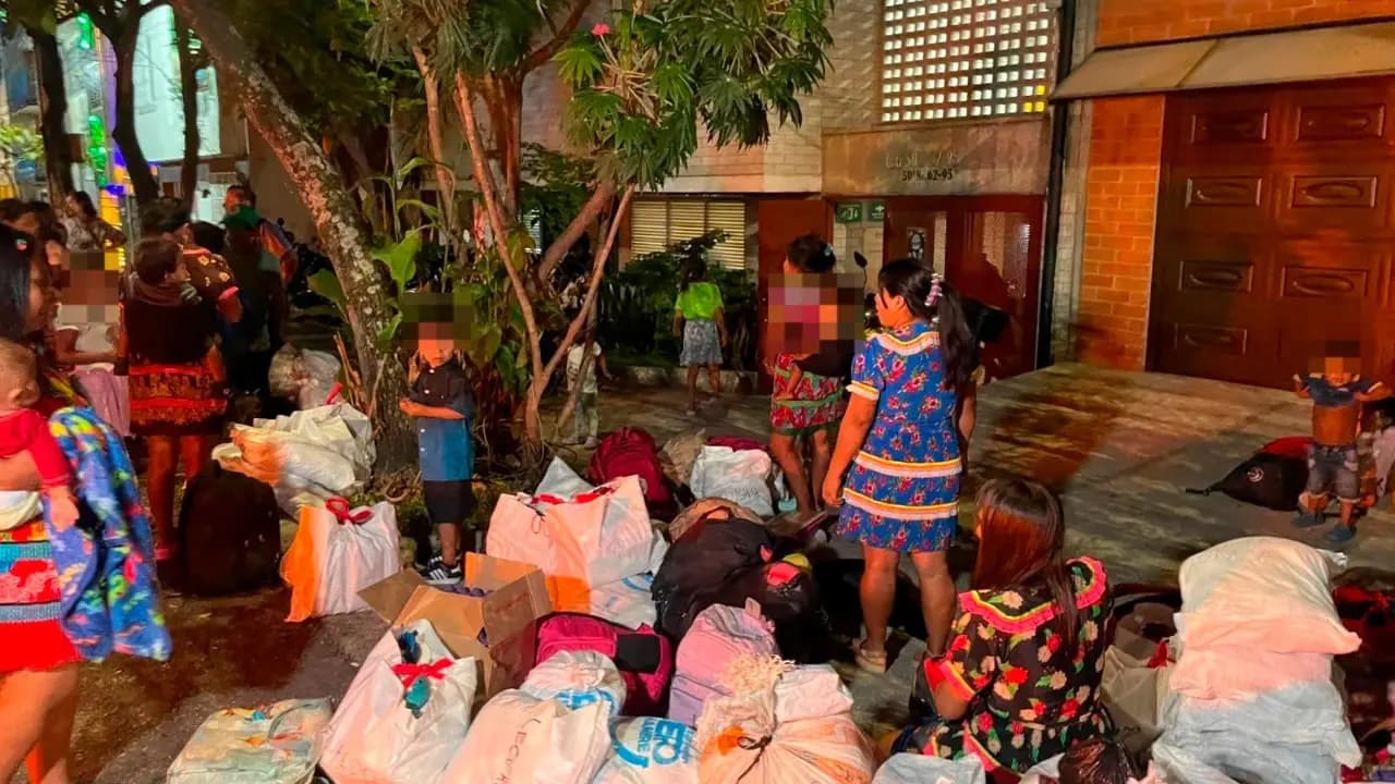 Familias indígenas emberá con sus bultos y costales amontonados en el andén de una calle de Medellín durante la noche