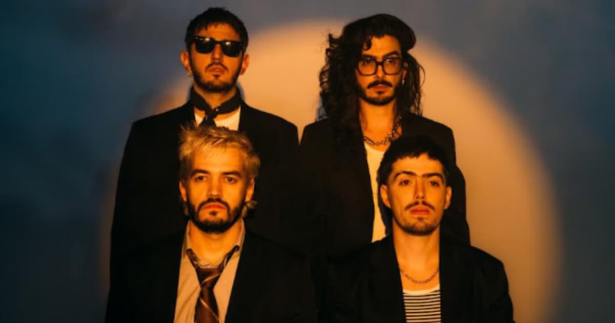Los cuatro integrantes de Morat, vestidos de negro, posan frente a una pared azul iluminada por un círculo de luz cálida