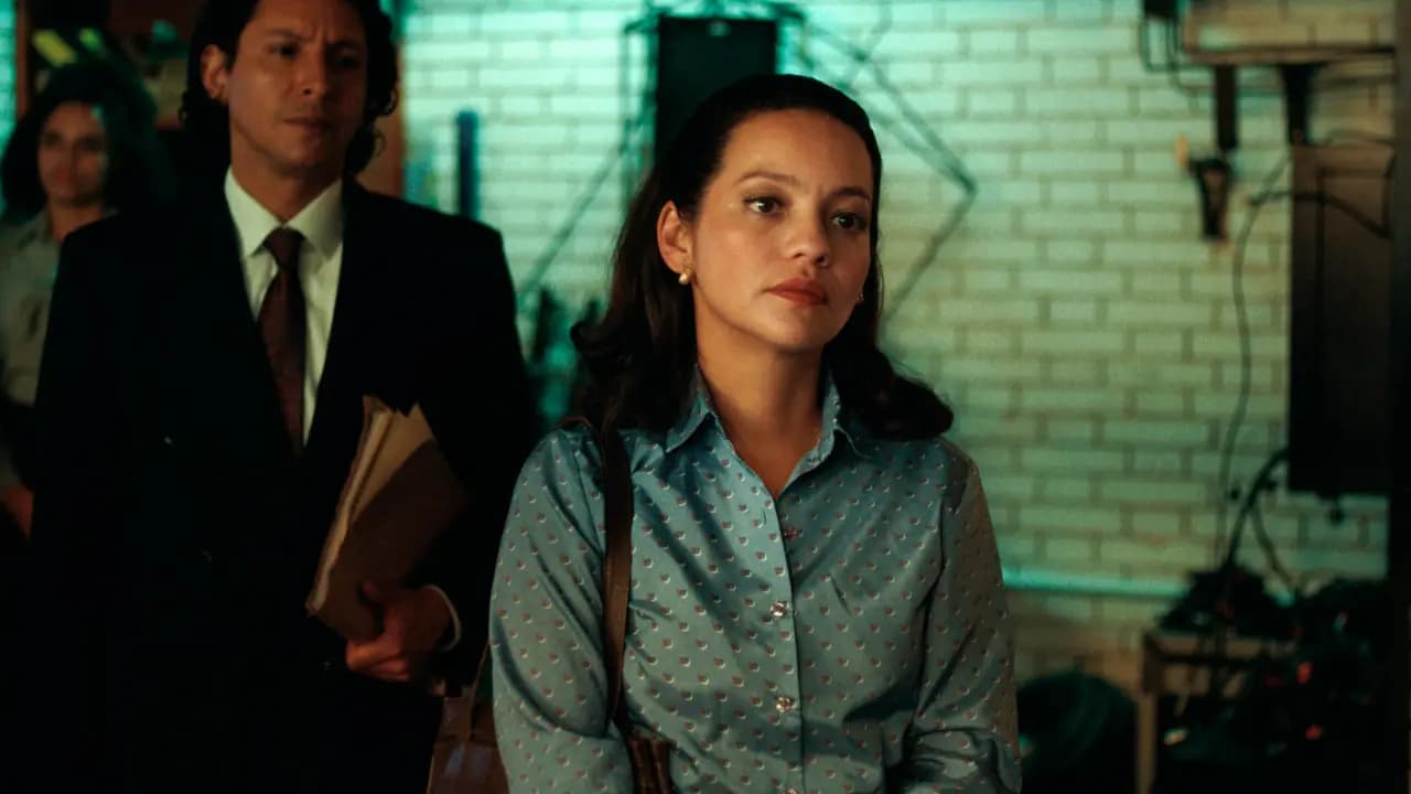 Natalia Reyes, con blusa azul de época, en una escena de la serie «Palacio»; detrás, un hombre de traje sostiene unas carpetas