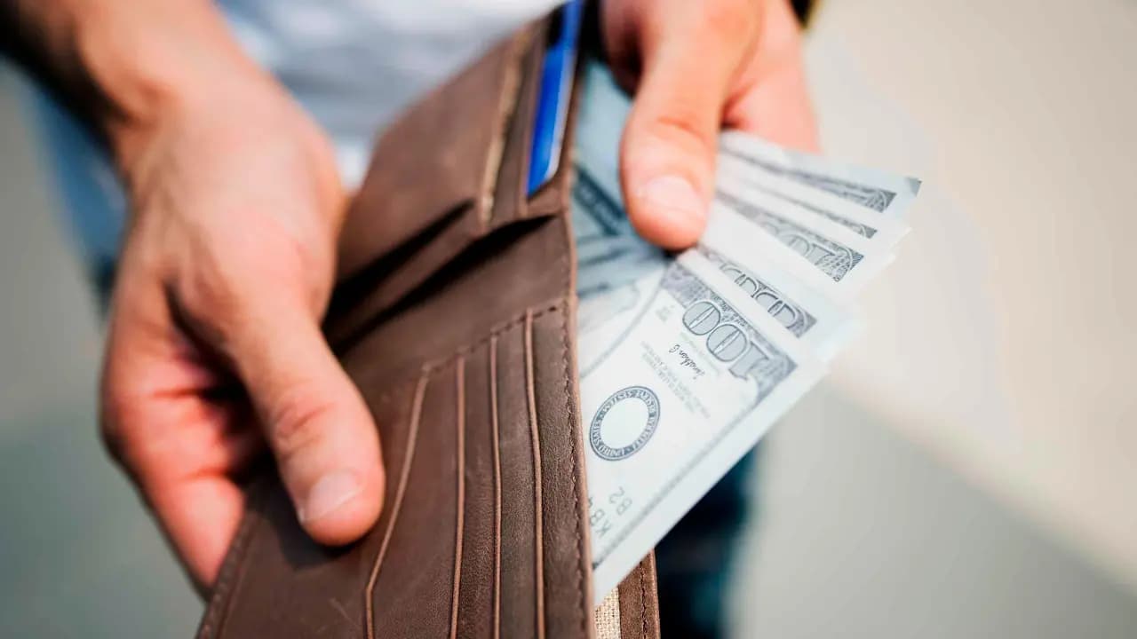 Una persona saca billetes de cien dólares de su billetera
