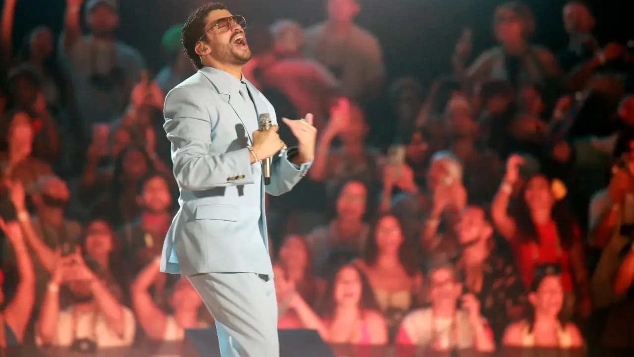 Bad Bunny canta en el escenario con traje azul claro frente a una pantalla con el público