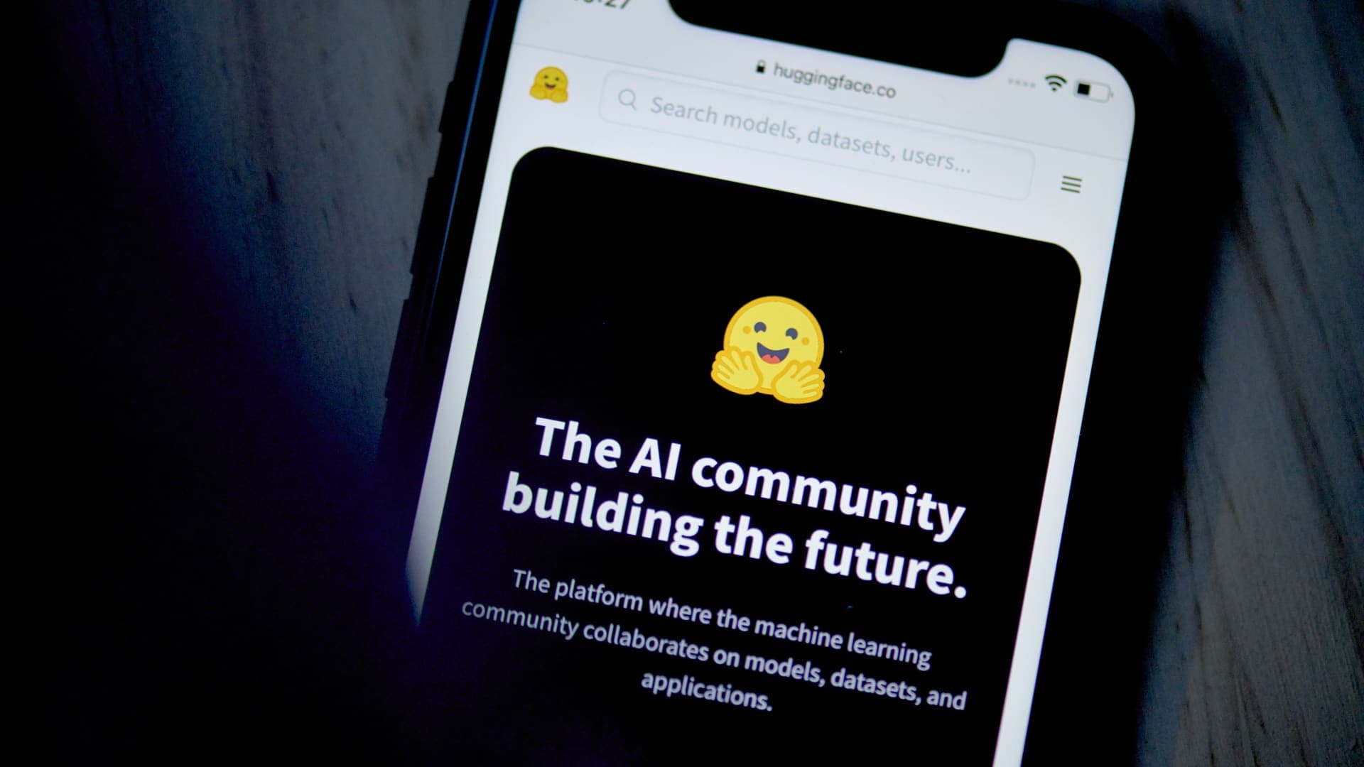 Un teléfono móvil muestra la página de inicio de la plataforma Hugging Face sobre una superficie oscura