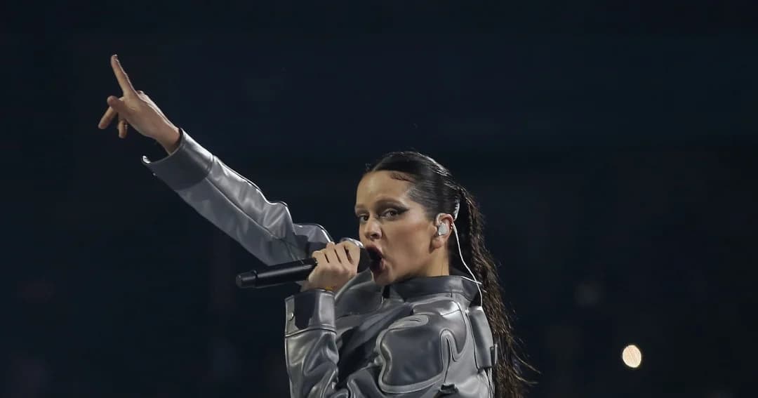 Rosalía canta en un concierto con chaqueta plateada y el brazo en alto