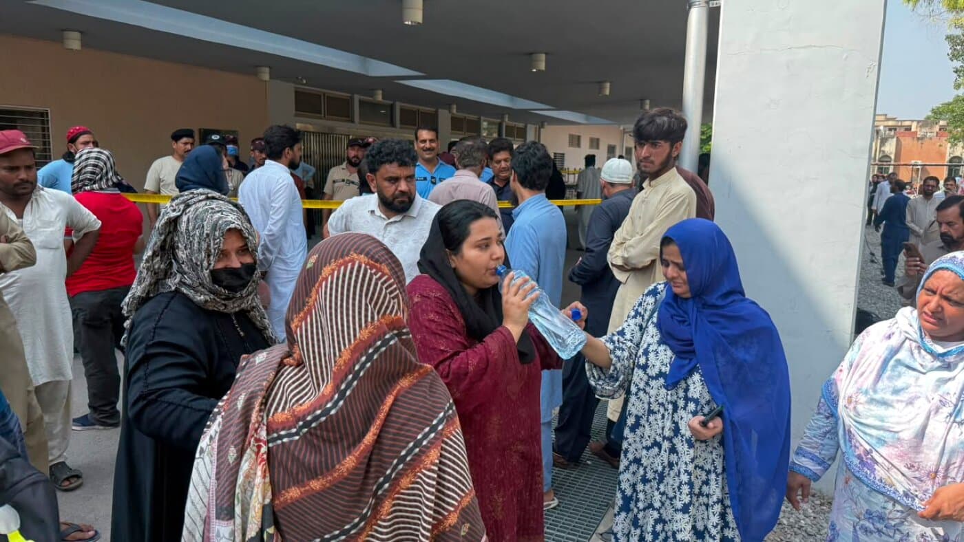 Familiares de los bebés muertos se agolpan a la entrada de un pabellón del hospital de Islamabad, tras una cinta amarilla de acordonamiento, mientras una mujer bebe agua de una botella