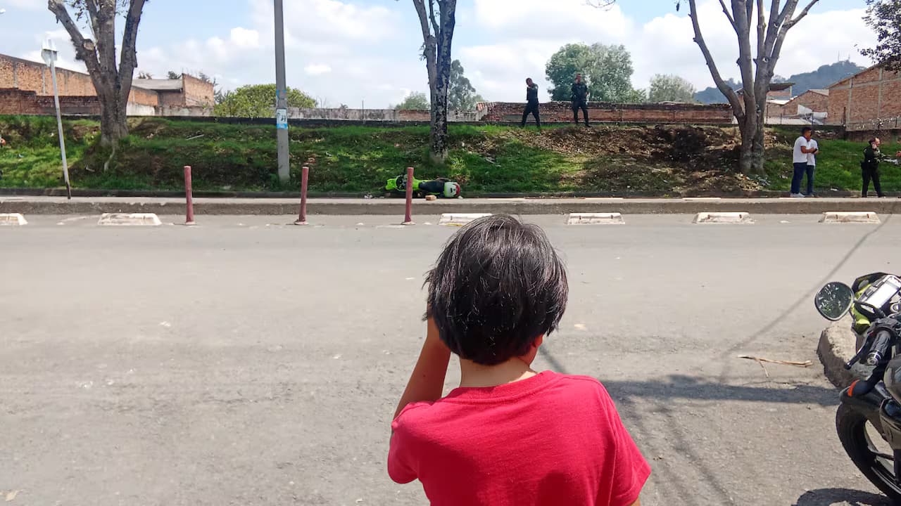 Un niño observa a policías y una motocicleta caída en el lugar del ataque en Popayán